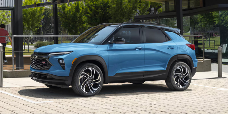 Light blue Chevrolet Trailblazer parked on a paved lot with trees and buildings in the background.