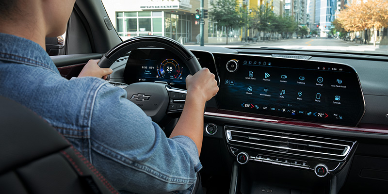 A person driving a Chevrolet car, hands on the steering wheel, with a large infotainment screen showing various apps.