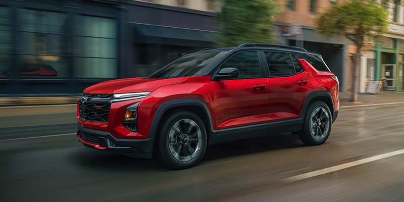 The new 2024 Chevrolet Trax RS in radiant red with black trim, driving on a wet city street.