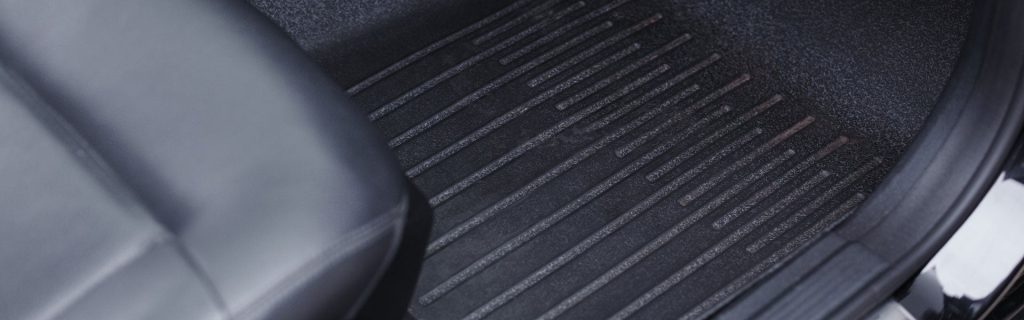 Close-up of a dark grey, ridged, rubber car floor mat and the edge of a black leather car seat.