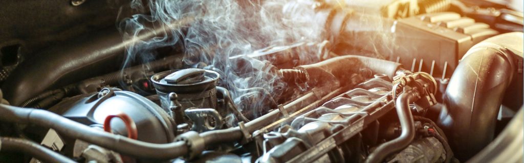A close-up of a steaming car engine, with various pipes and components visible, suggesting overheating or a breakdown.