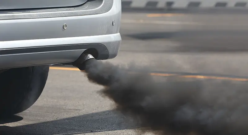 Close-up of a car's exhaust pipe spewing thick black smoke, indicative of pollution.
