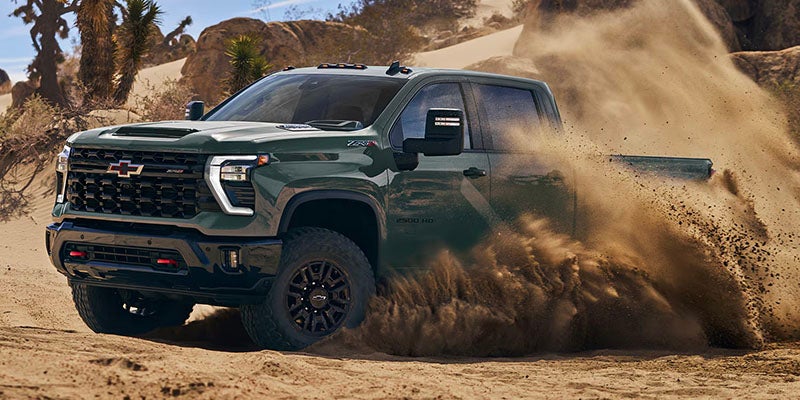 A dark green Chevrolet Silverado kicks up dust while driving across sandy terrain.